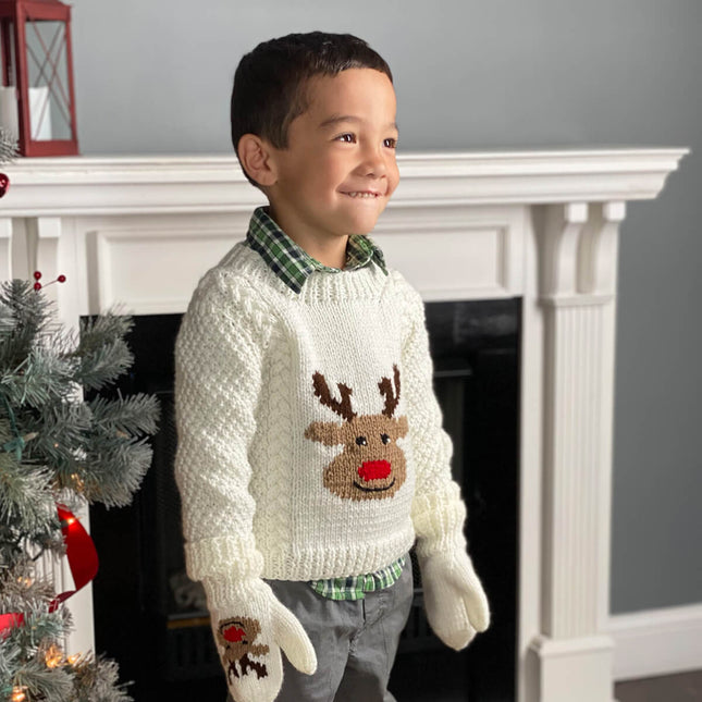 Child next to Christmas tree wearing a knit reindeer sweater with aran cables