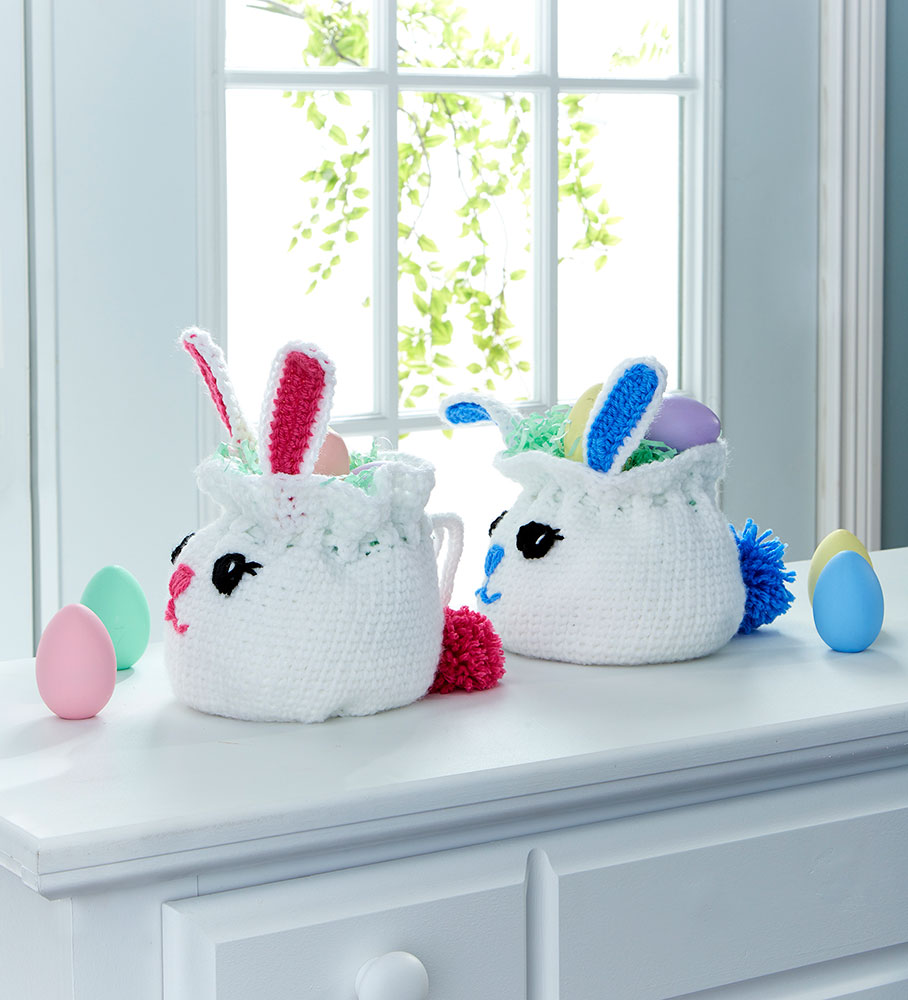 Two Bunny Bag Easter Baskets side view and easter eggs, one with pink ears, nose, and pom pom tail, and one with Blue. 